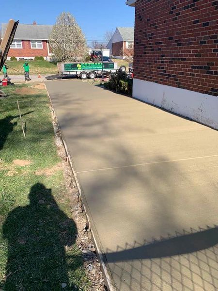 New concrete walkway next to a brick building; construction equipment in the background.