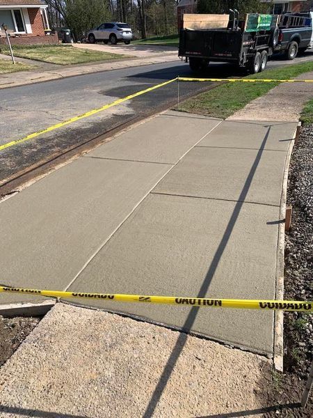 Freshly poured concrete driveway with safety tape, next to sidewalk. Truck in background.