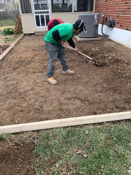 Two people are working on leveling dirt in an outdoor area. Green and red shirts, gray pants.