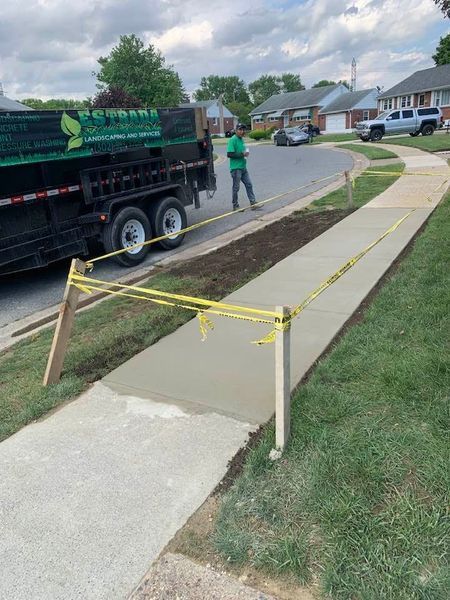 Newly poured concrete sidewalk with caution tape; landscaping truck and worker visible.