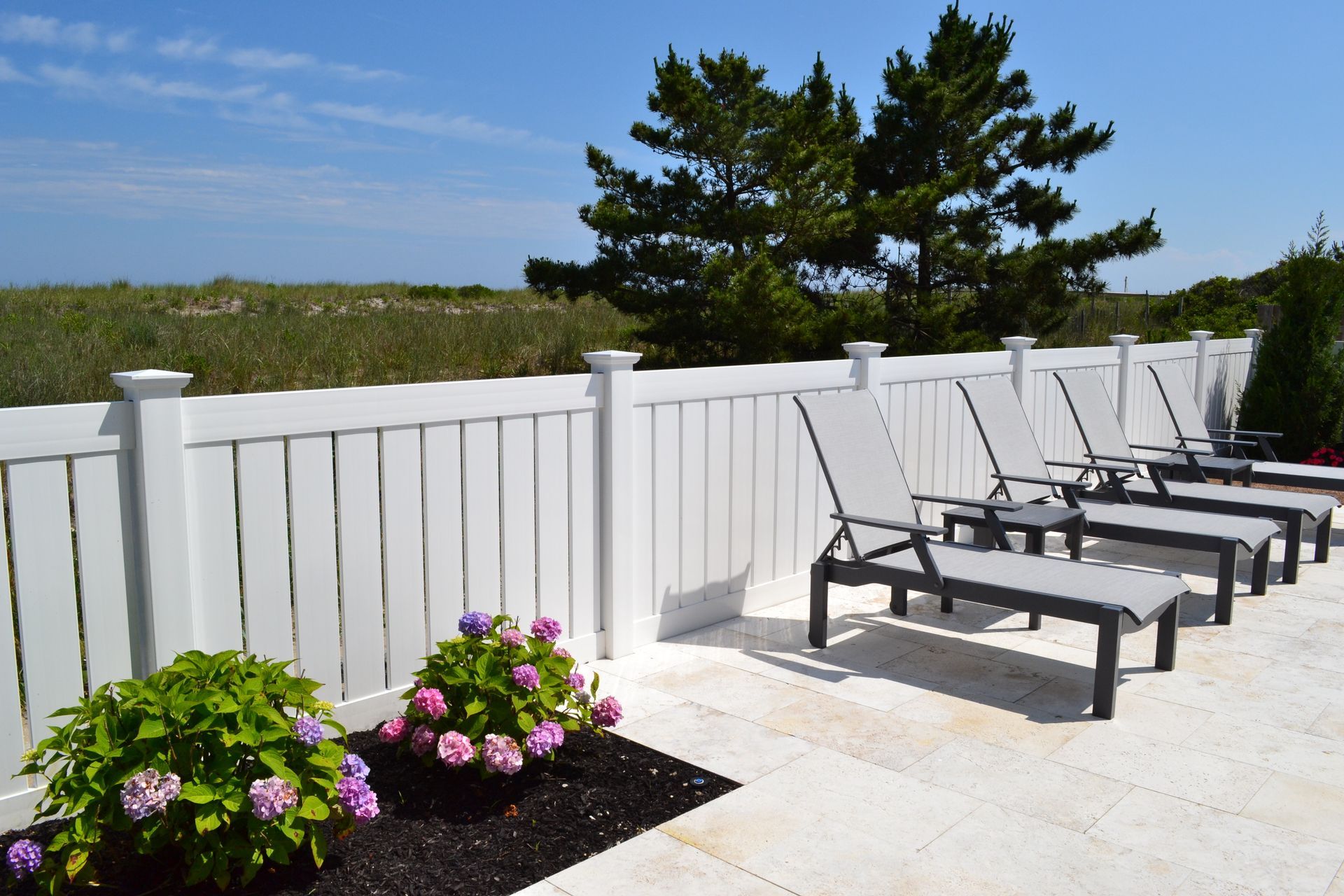 Wooden fence surrounding a grassy yard with a white house and blue sky in the background.