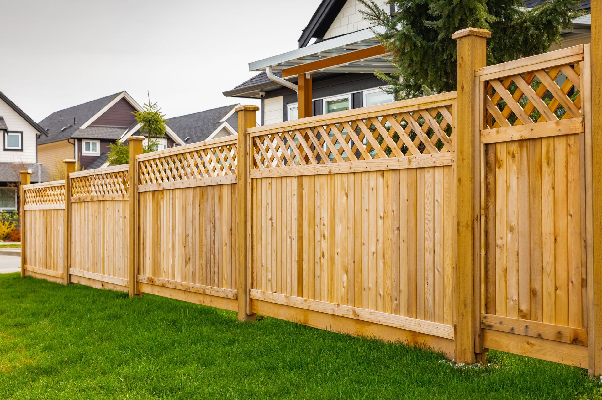 Wooden fence with lattice top, surrounding a green lawn with houses in the background.