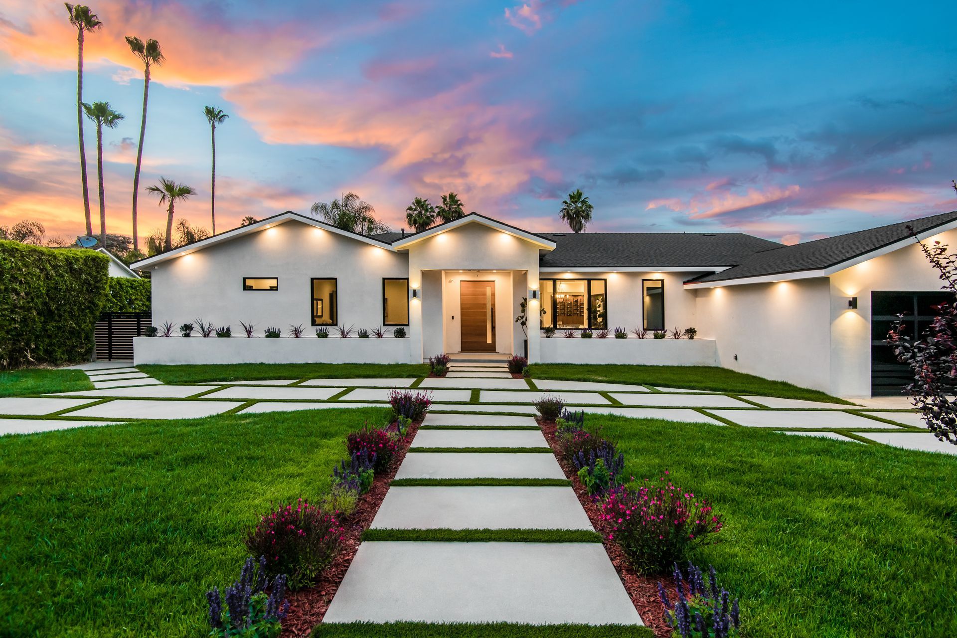 White modern home with a walkway, green grass, and vibrant sunset sky.