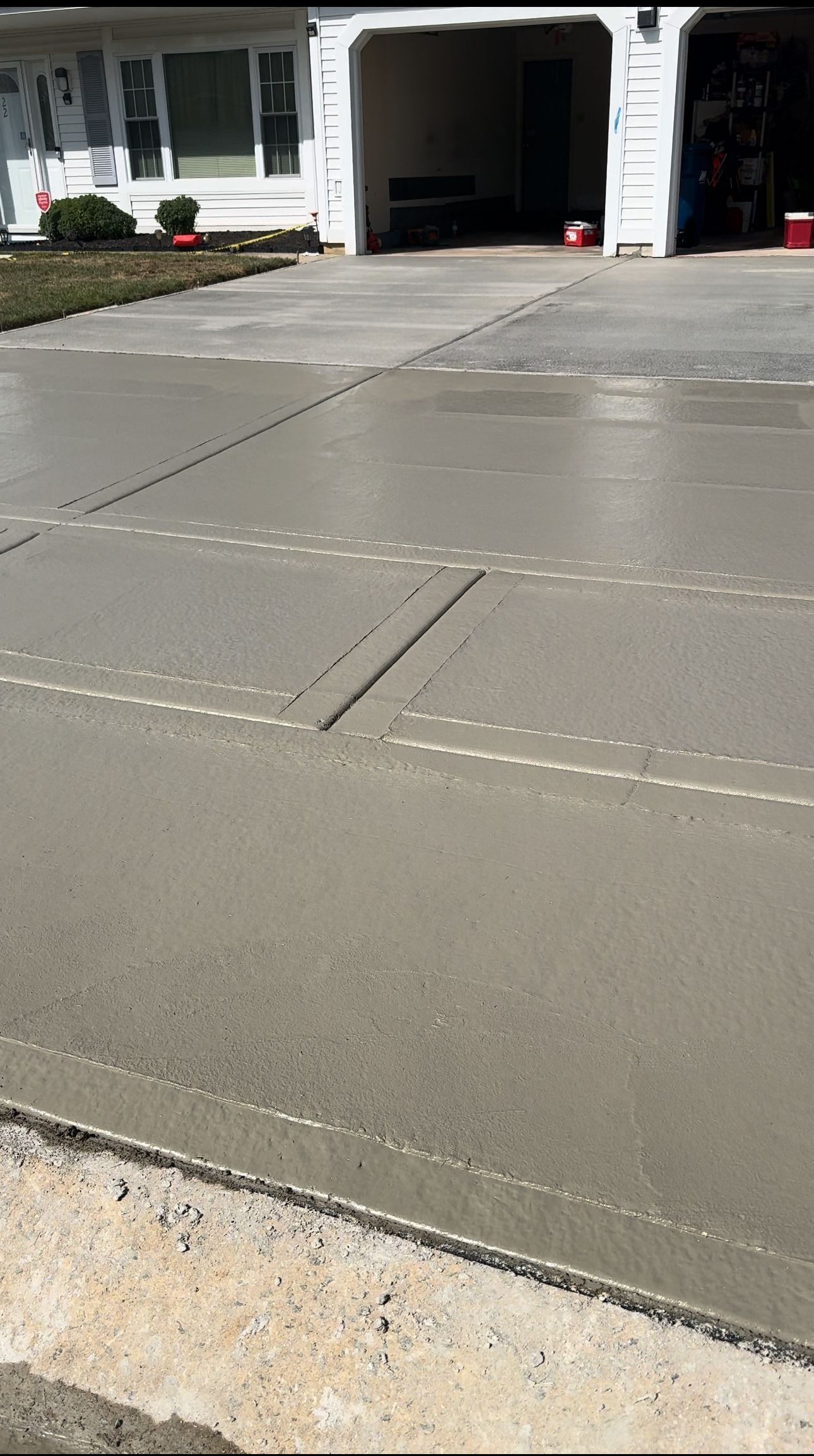 Freshly poured concrete driveway in front of a white house with a garage.