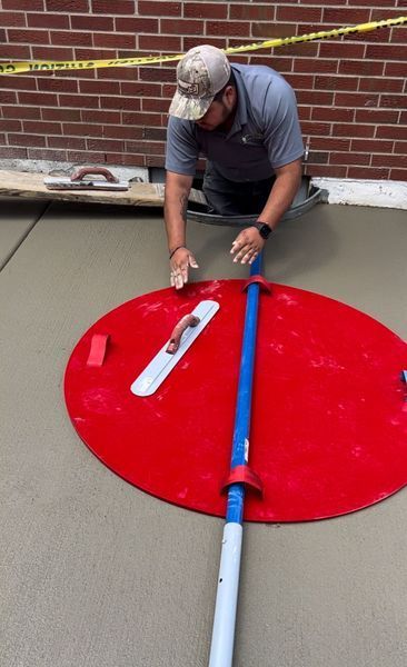 Man kneeling, using a red tool to smooth wet concrete. A brick wall is in the background.
