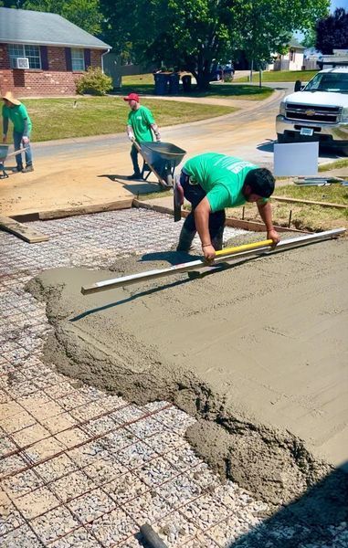 Construction workers leveling wet concrete with a screed. Others use a wheelbarrow and shovel.