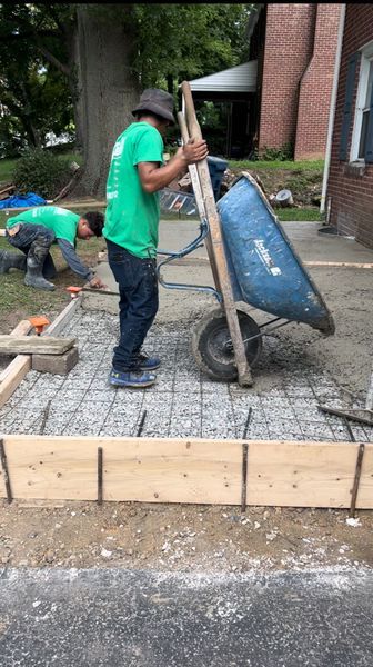 Construction worker pushing wheelbarrow on concrete forms, another worker in background.