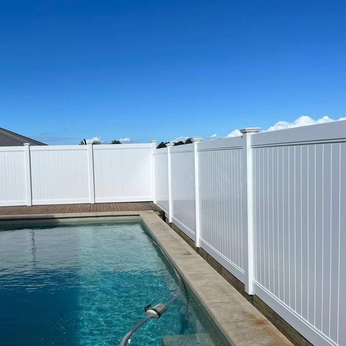 a white fence surrounds a swimming pool on a sunny day .