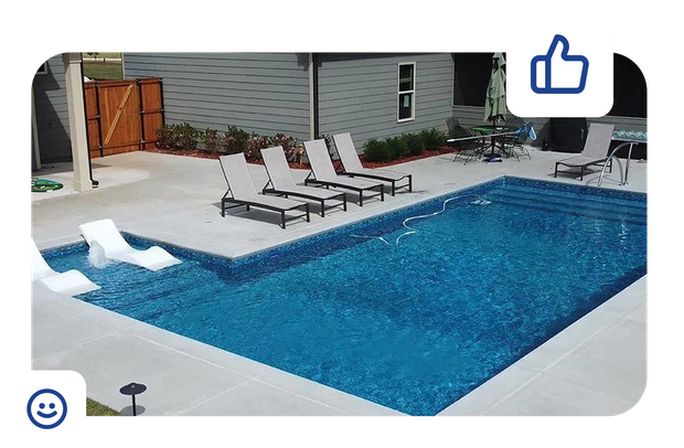 Blue-tiled swimming pool surrounded by a concrete deck, set against a backdrop of green hedges.