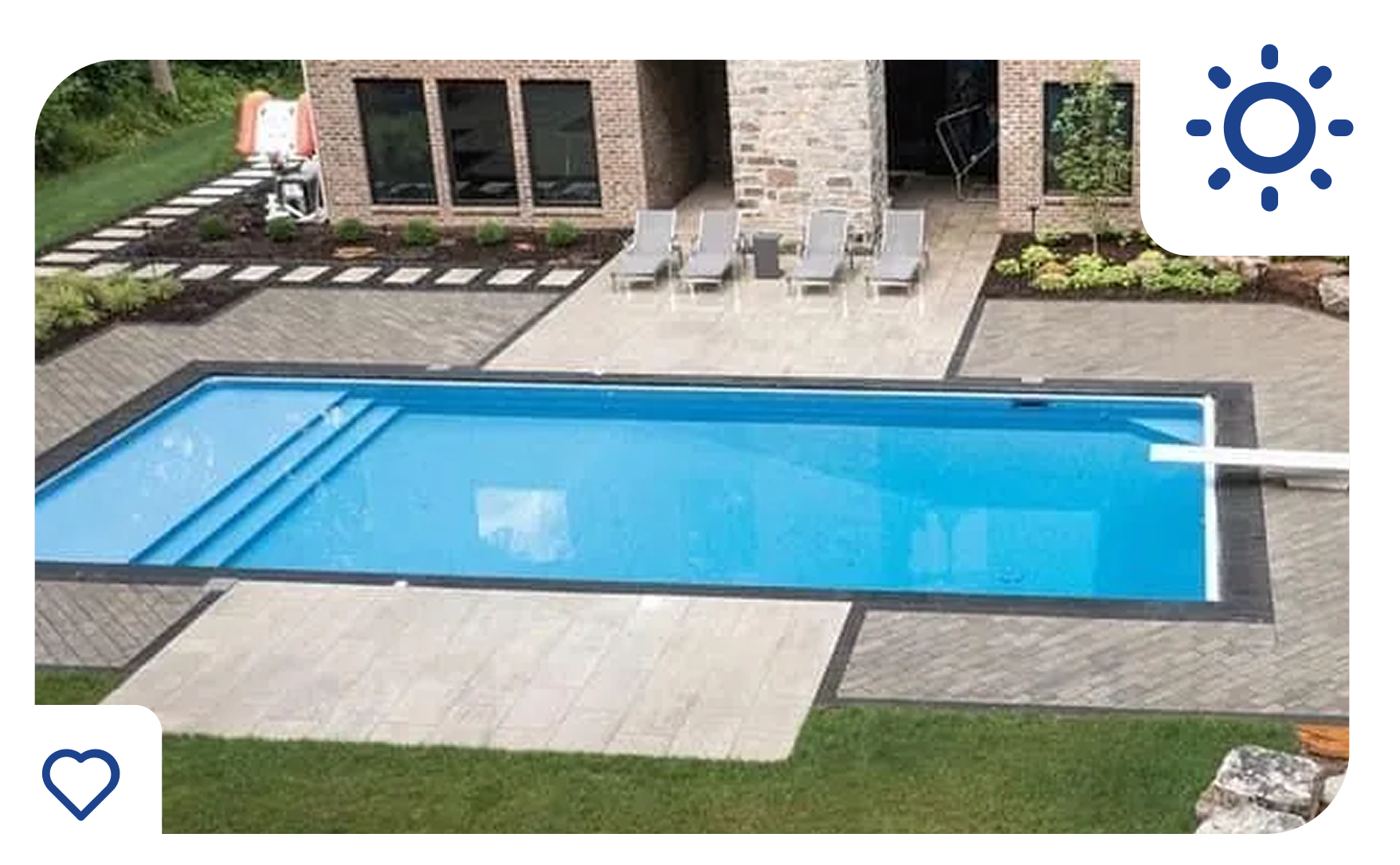 Rectangular swimming pool in a backyard with stone patio, lounge chairs, and building with windows.