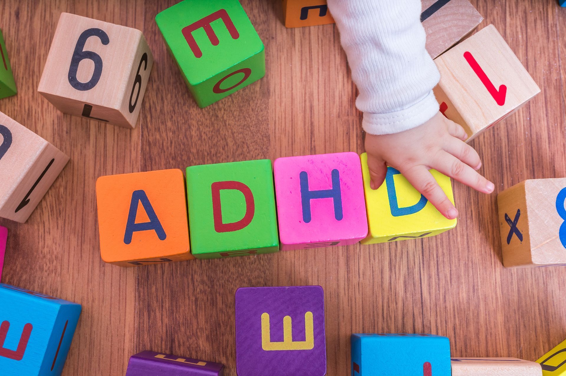 A child's hand reaches for the letters ADHD, illustrating Child Attention Deficit Hyperactivity Disorder in Eagle River, AK.