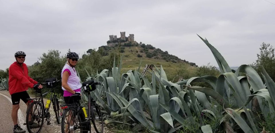 Two people on bikes with Almodovar Castle in the background on a cloudy day