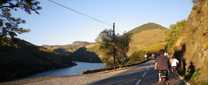 A group of cyclists on a quiet road along the river in the Douro valley, Portugal.