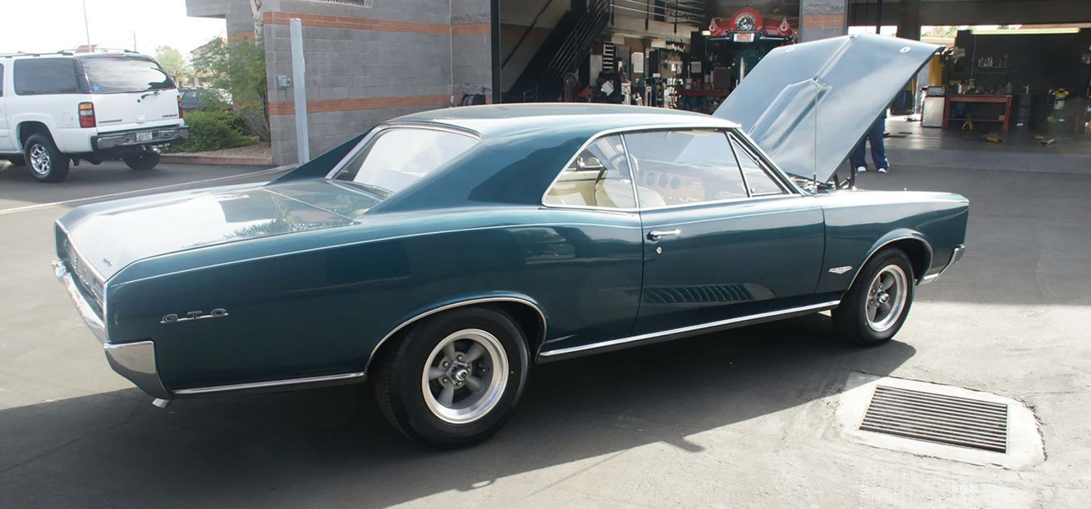A blue car with the hood up is parked in a parking lot
