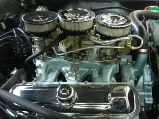 A close up of a car engine with three carburetors