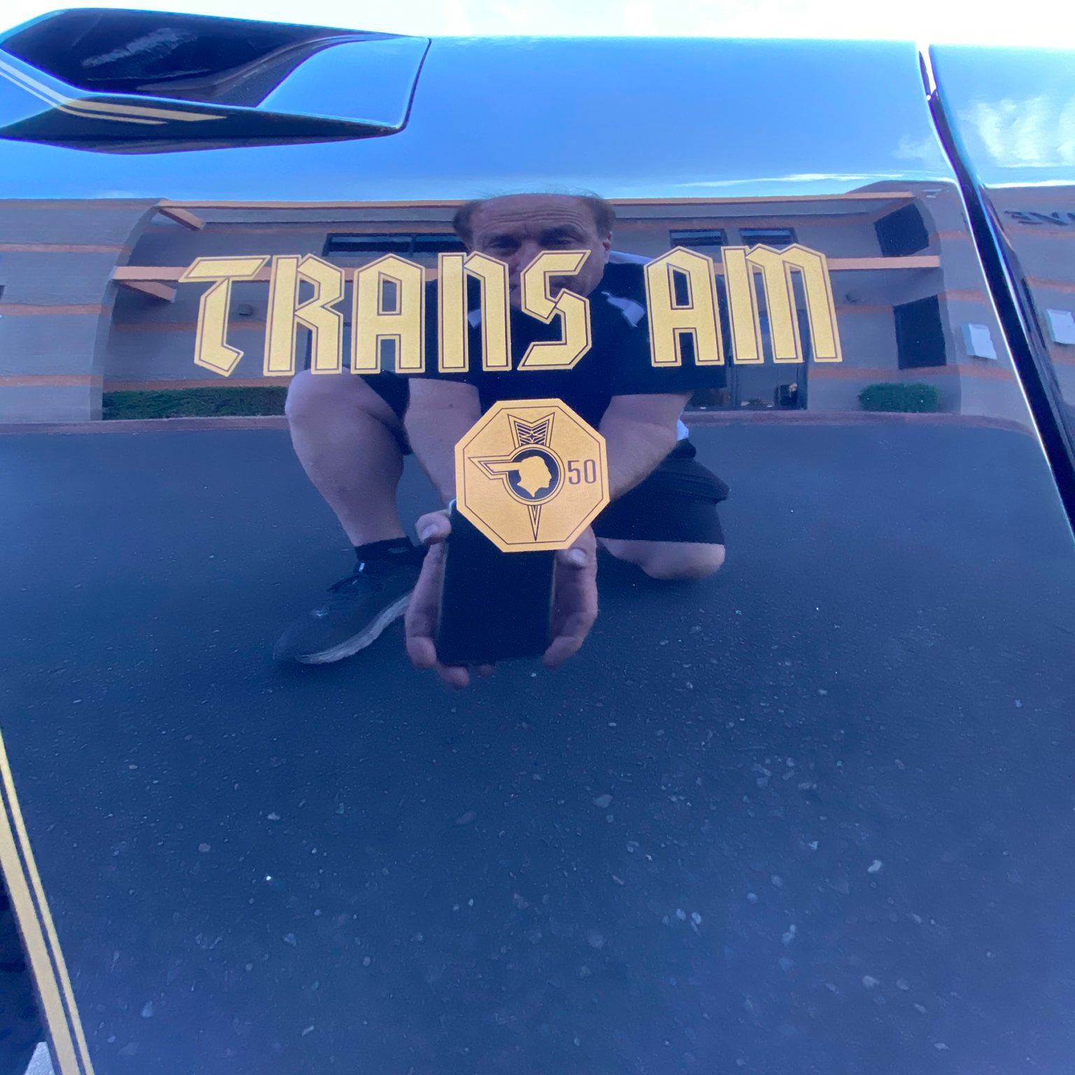 A man is kneeling down in front of a car that says trans am