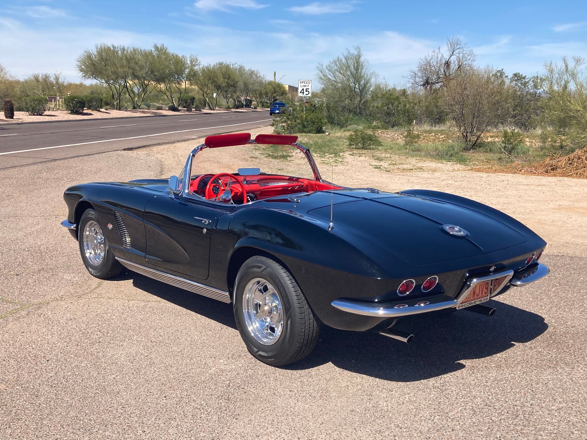 A black corvette convertible is parked on the side of the road.