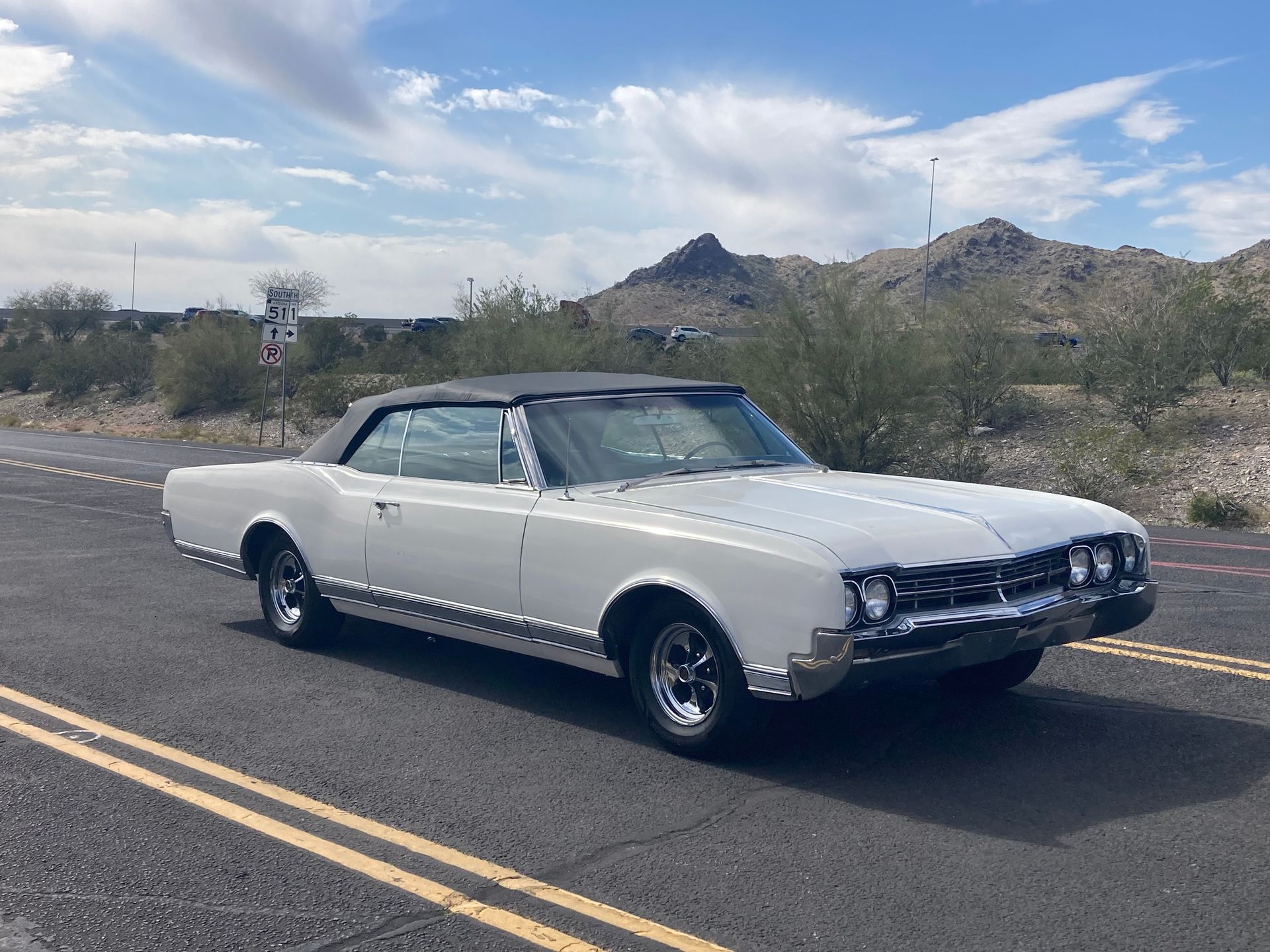 A white oldsmobile cutlass convertible is parked on the side of the road.