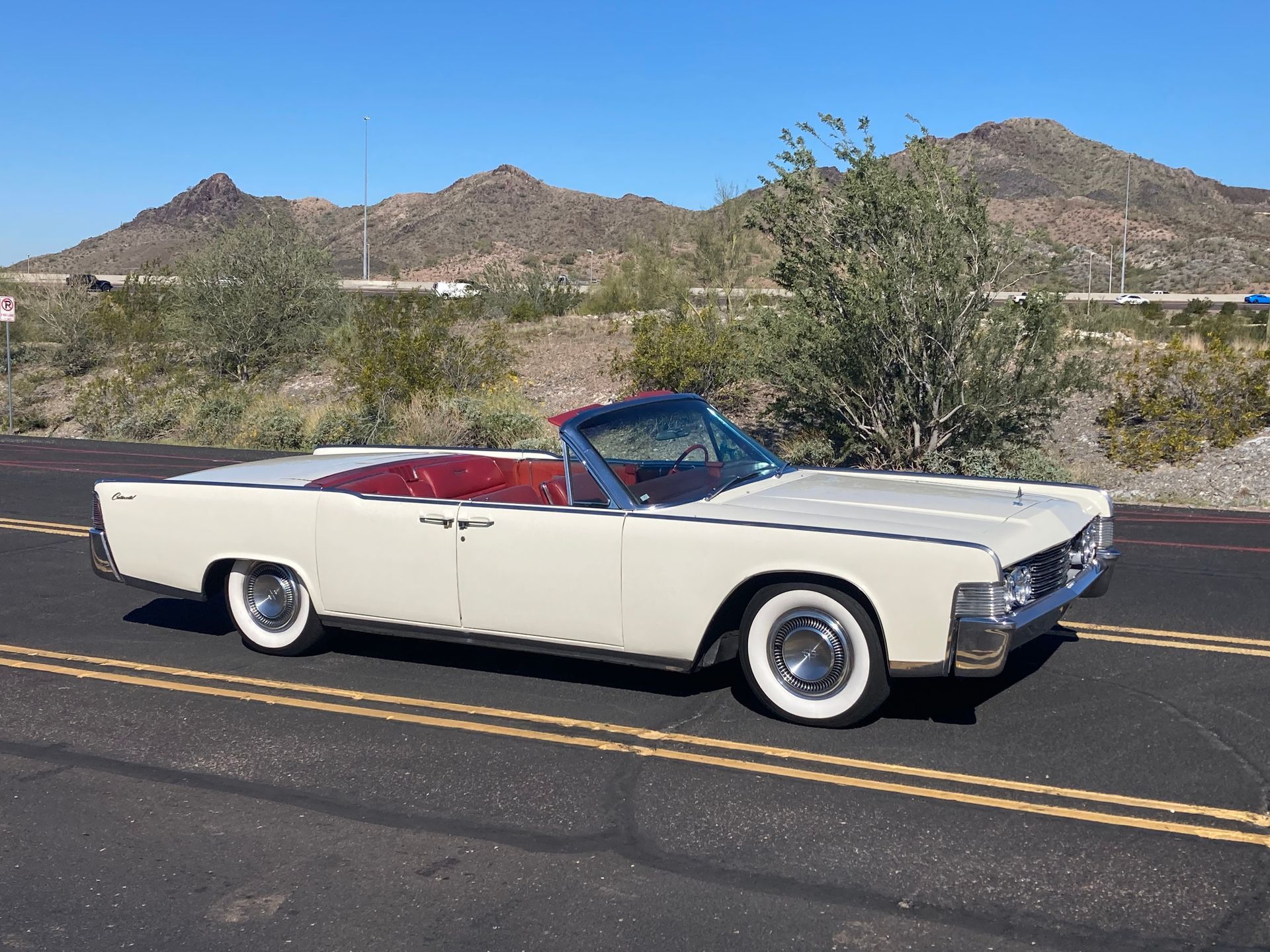 A white car is driving down a road with mountains in the background.