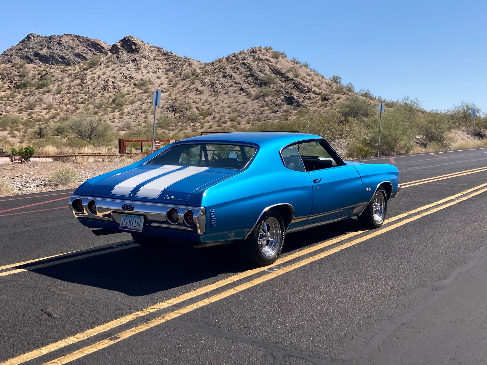 A blue car with white stripes is parked on the side of the road