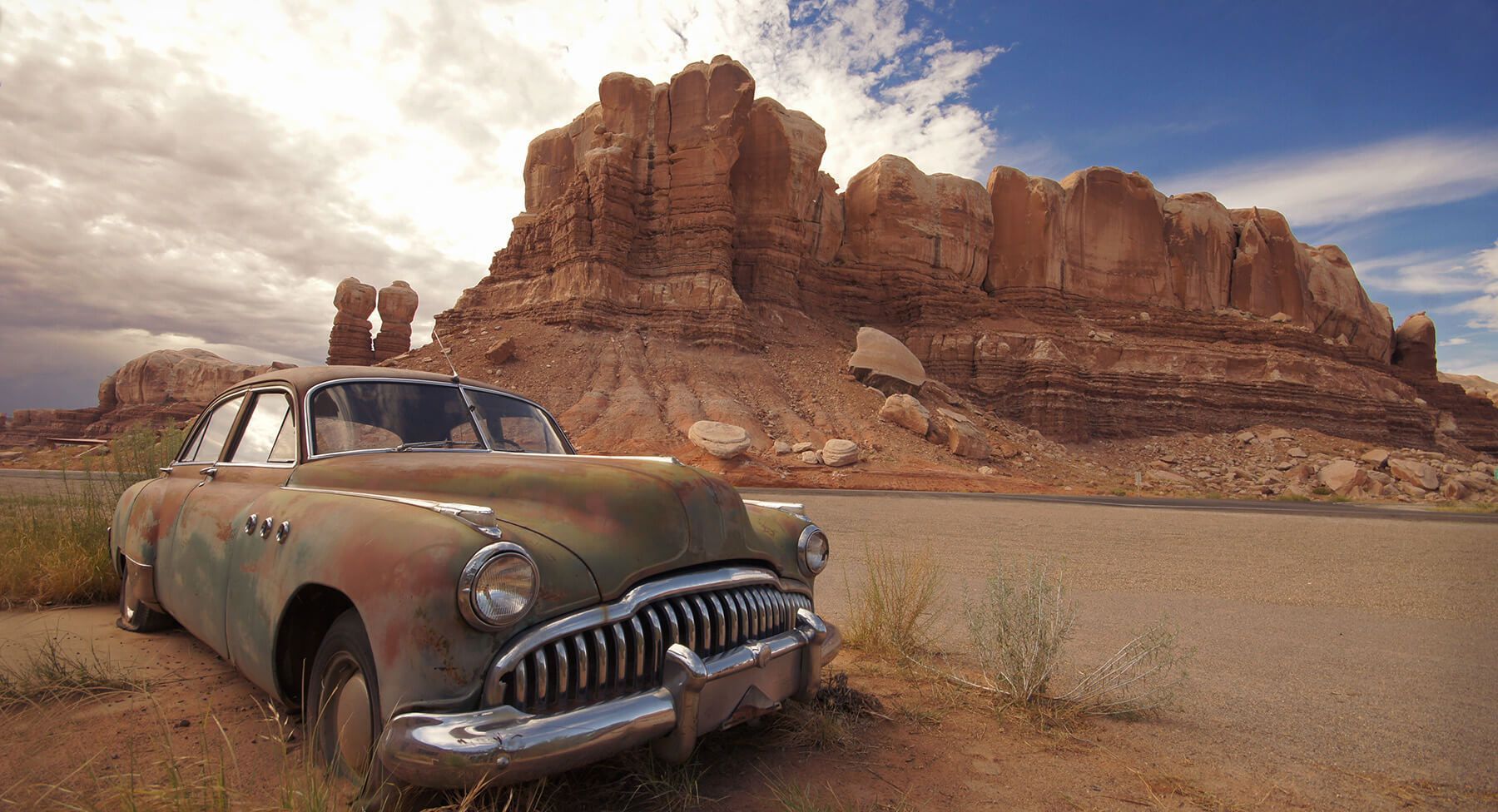 An old rusty car is parked on the side of the road in the desert.