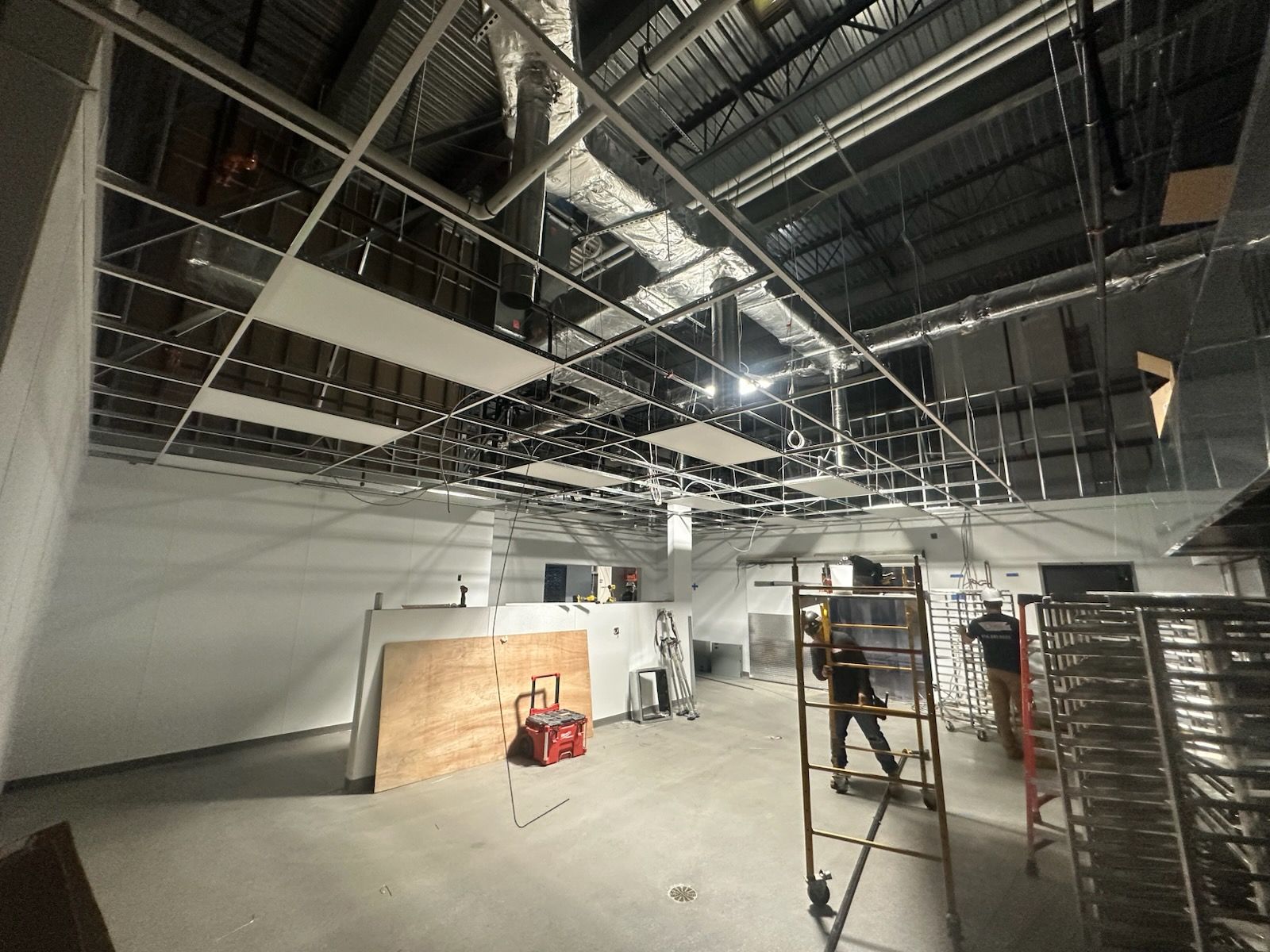Interior construction site with exposed ceiling grid, workers, and unfinished walls.
