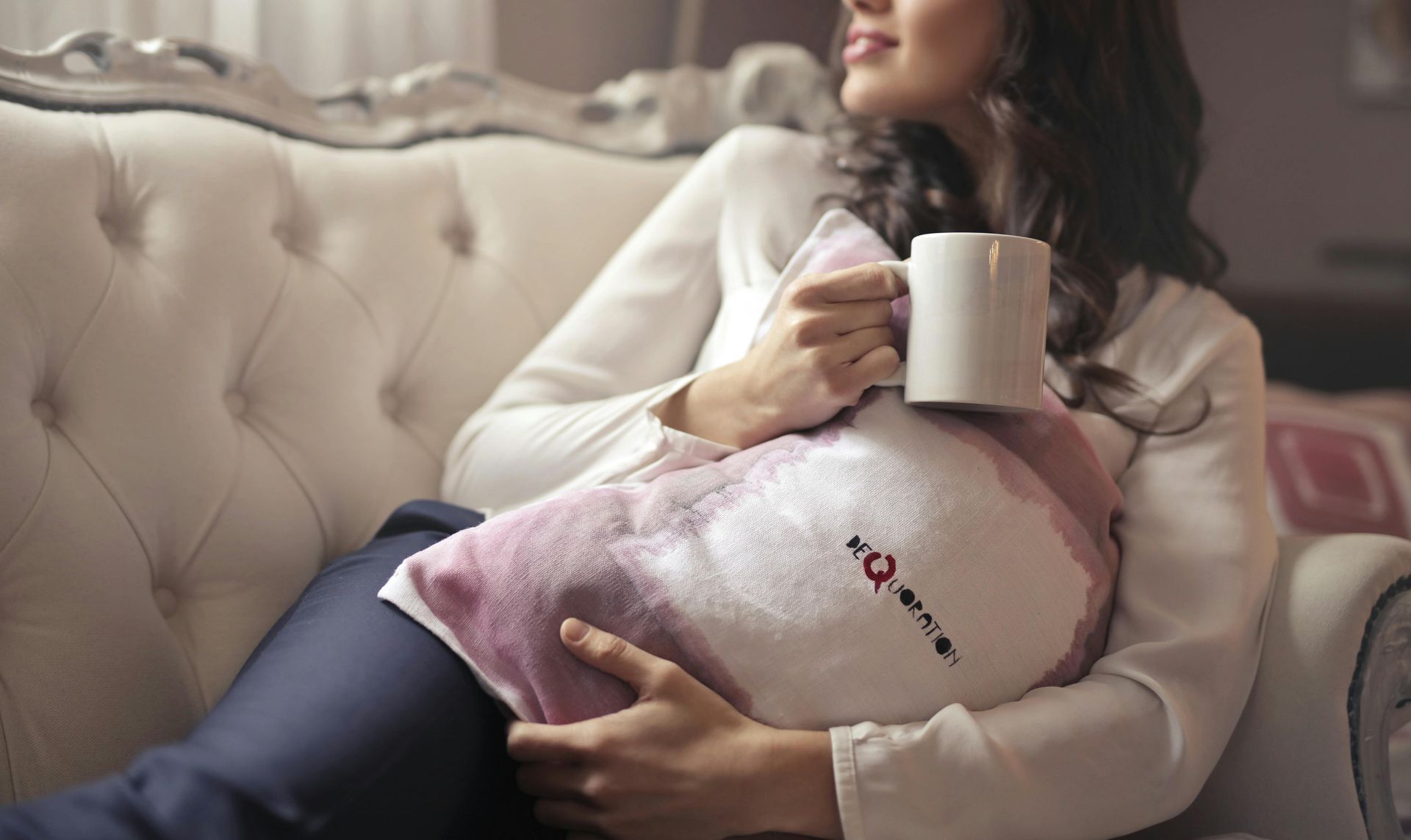 A woman is sitting on a couch holding a cup of coffee.