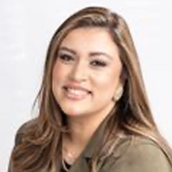 Tati smiling, wearing a green blazer, against a white backdrop.