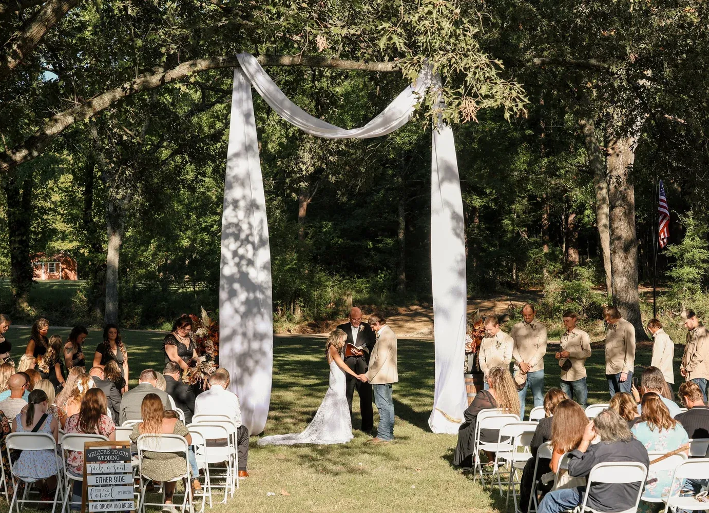 A historic stone church with a wooden door and arched windows, surrounded by lush green trees under a blue sky.