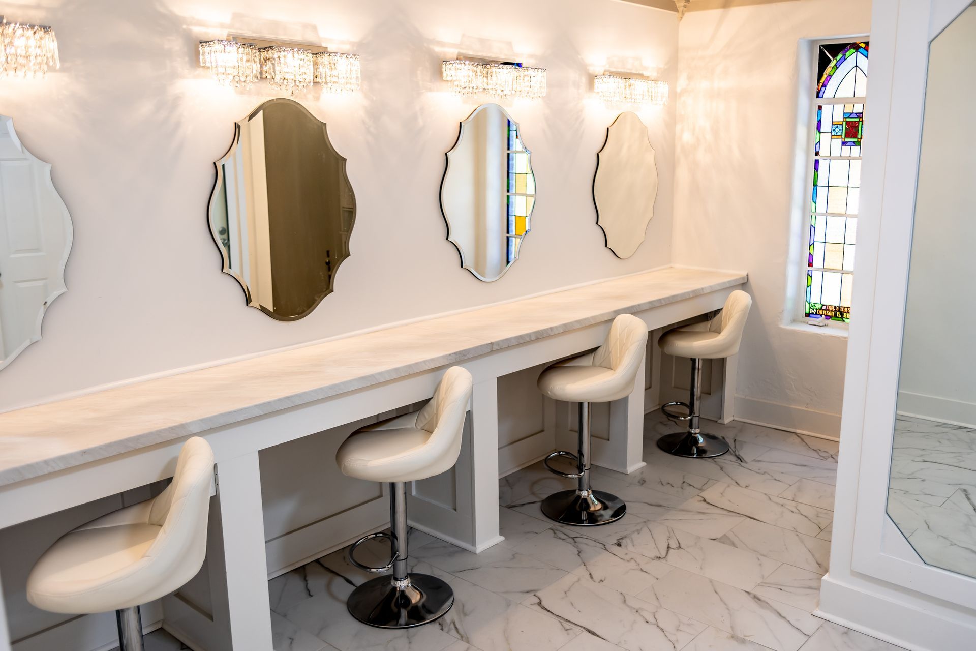 A salon workspace with two black chairs, mirrors, and a beverage cooler built into a dark countertop.
