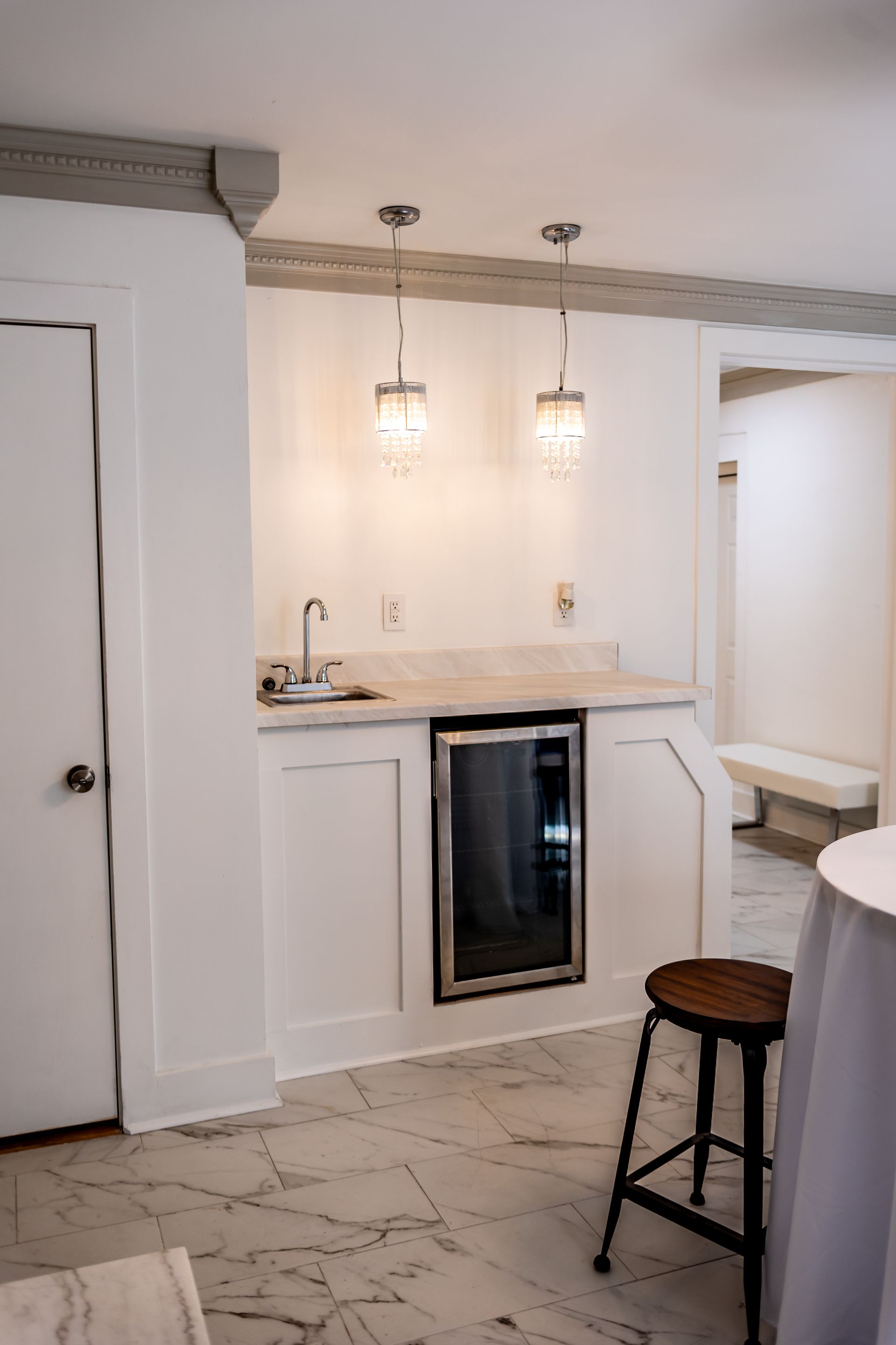 A stainless steel commercial ice machine with a black top unit, filled with ice and a white scoop, against a tiled wall.