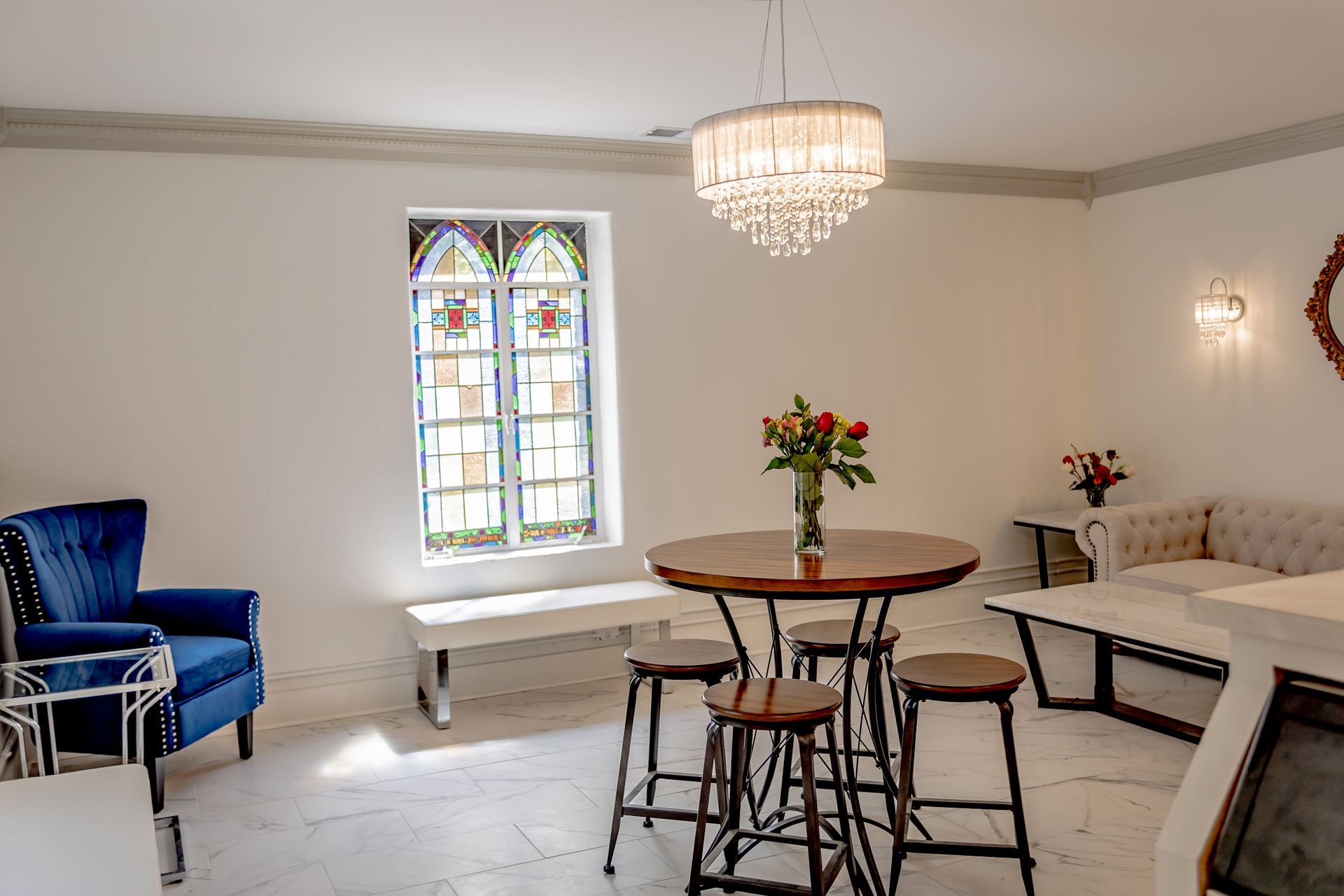 A meeting room set for a presentation with multiple round tables with white tablecloths, wooden chairs, and speakers.