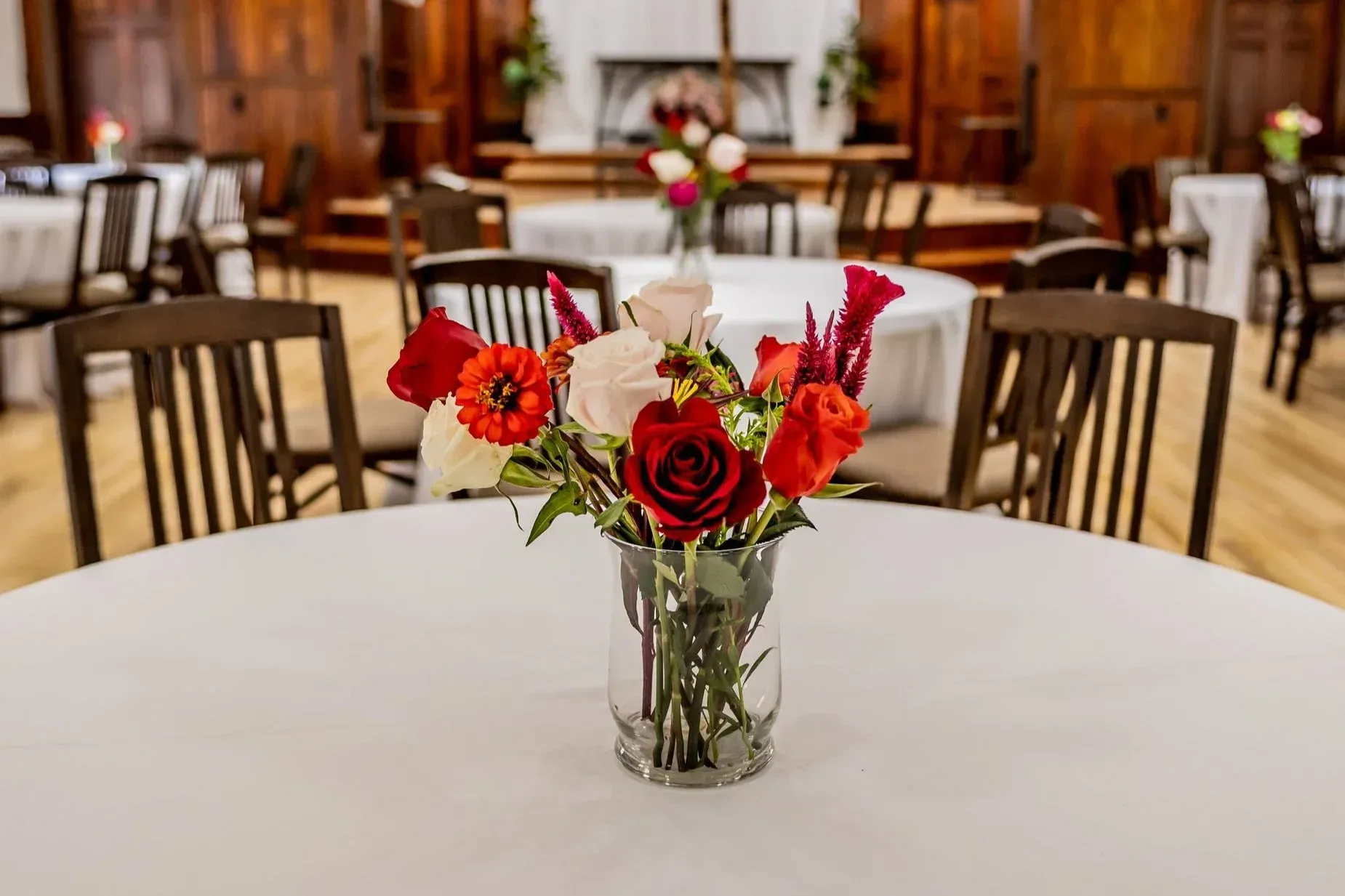 A bartender in a vest and bowtie pours a cocktail into a glass lined up on a bar at a social gathering.