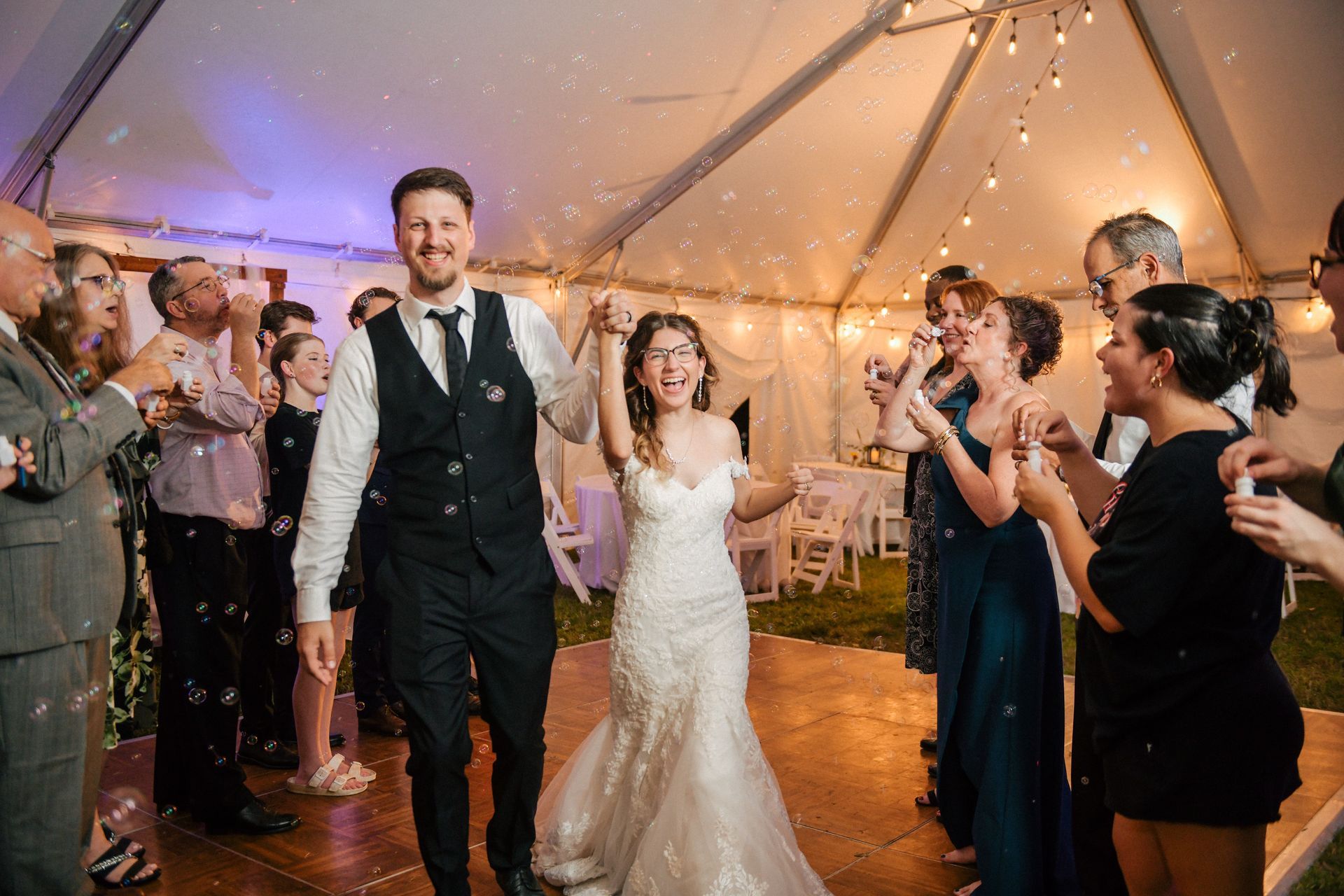 A wedding coordinator points toward the venue as a server stands by, with a couple in formal attire seated in front.