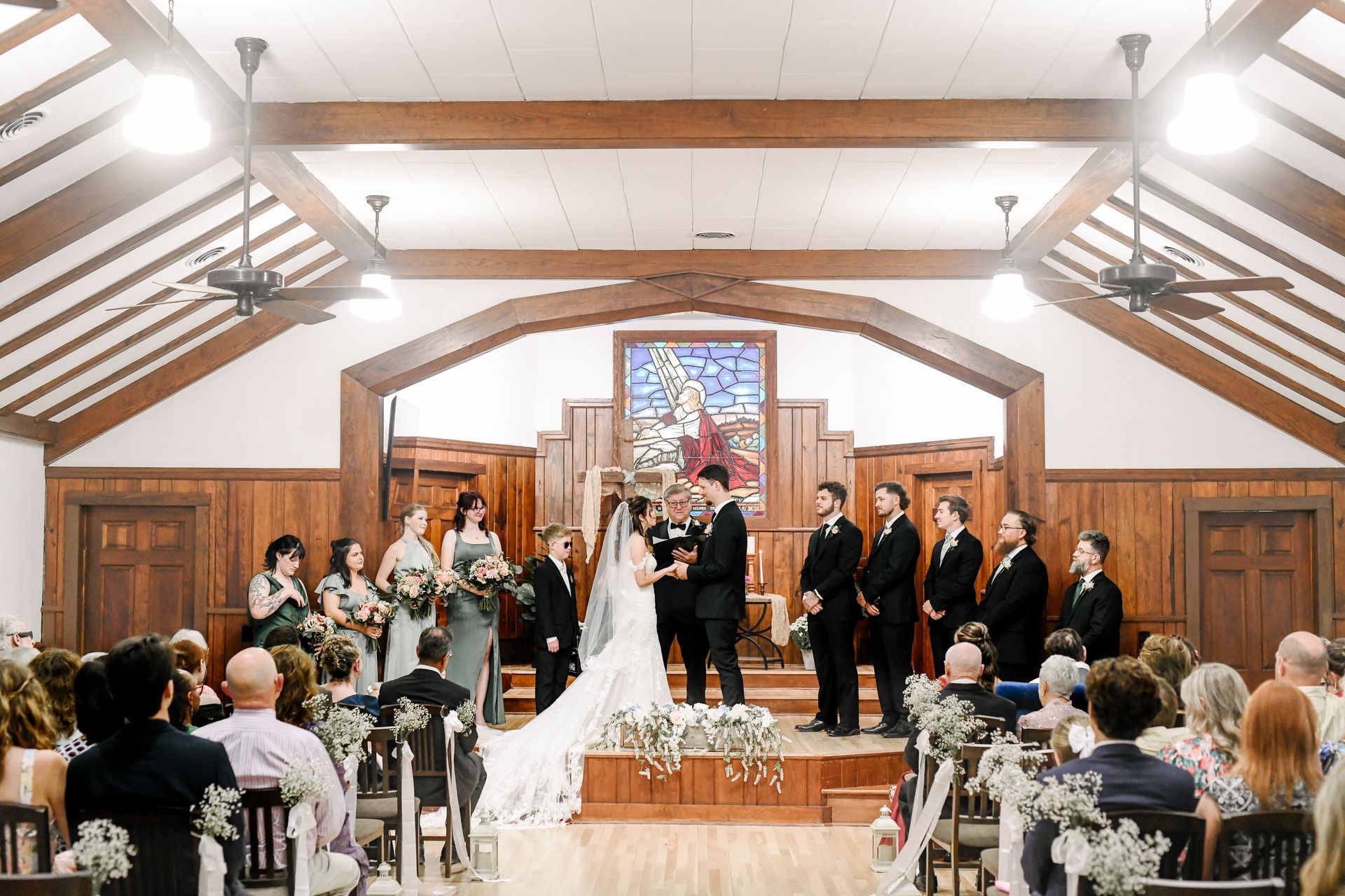 A group of people gathers in a warmly lit, rustic lounge, chatting and holding drinks around tables and a sofa.