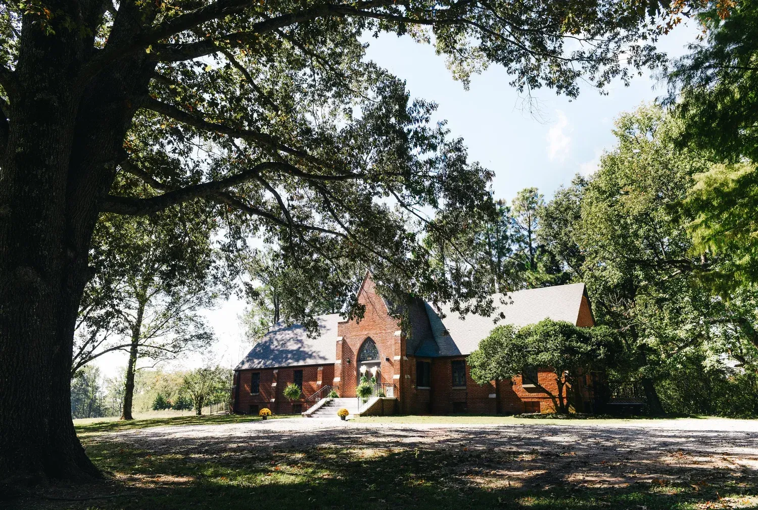 A brick church building nestled among large, leafy trees on a sunny day.