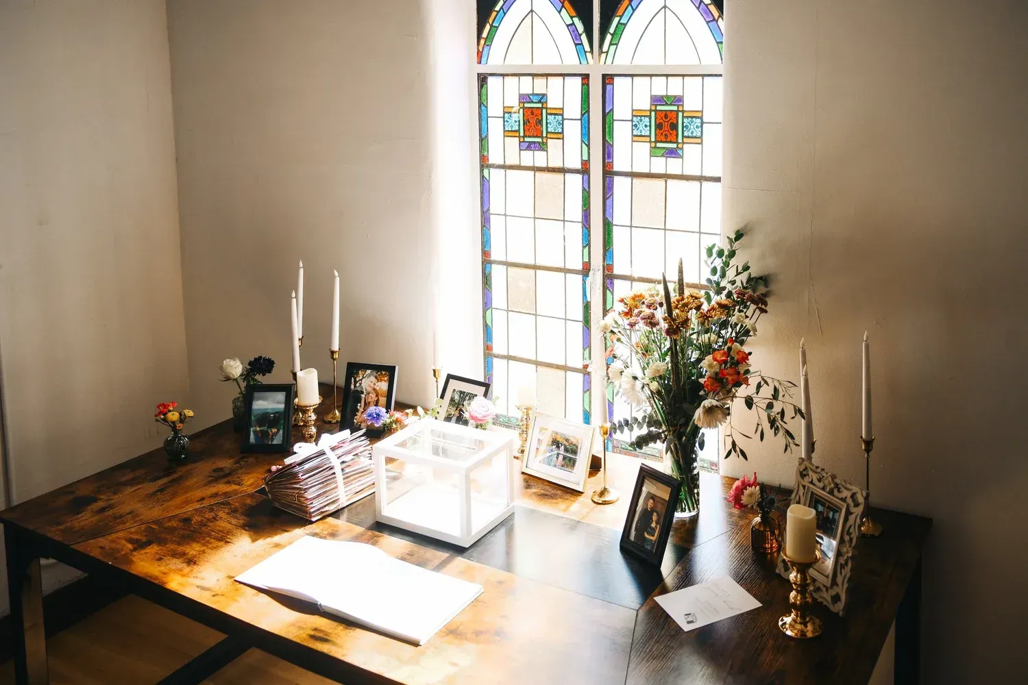 A couple stands under a draped fabric wedding arch in a wooded outdoor ceremony setting, facing a seated group of guests. A bride and groom exchange vows under a white draped archway in a tree-shaded outdoor setting with guests seated in chairs.