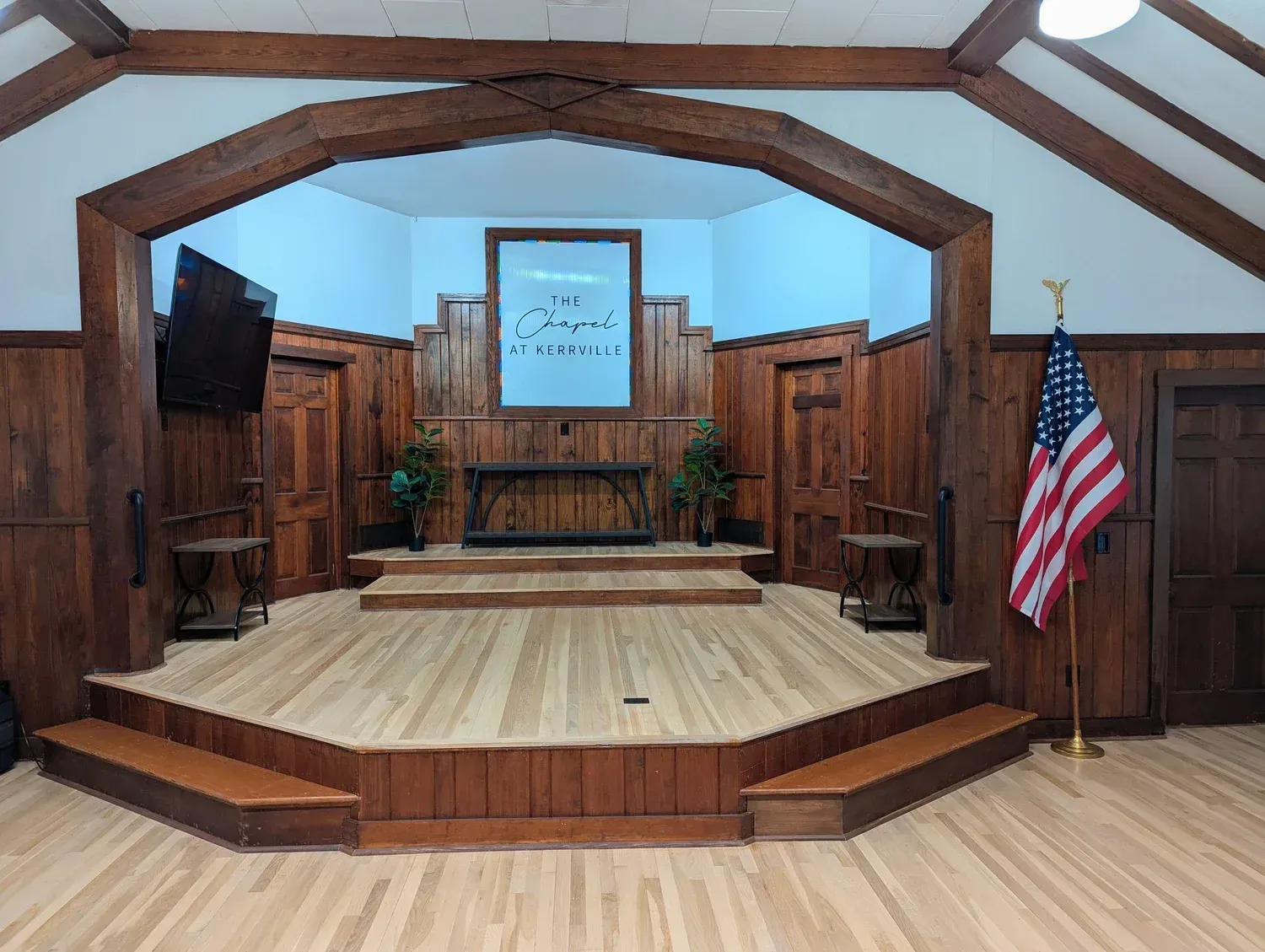 Two black PA speakers on tripod stands in an empty, minimalist room with purple accent lighting.
