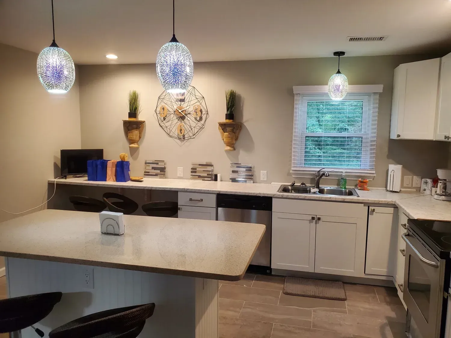 A modern kitchen with a granite-topped island, white cabinets, stainless steel appliances, and black stools.