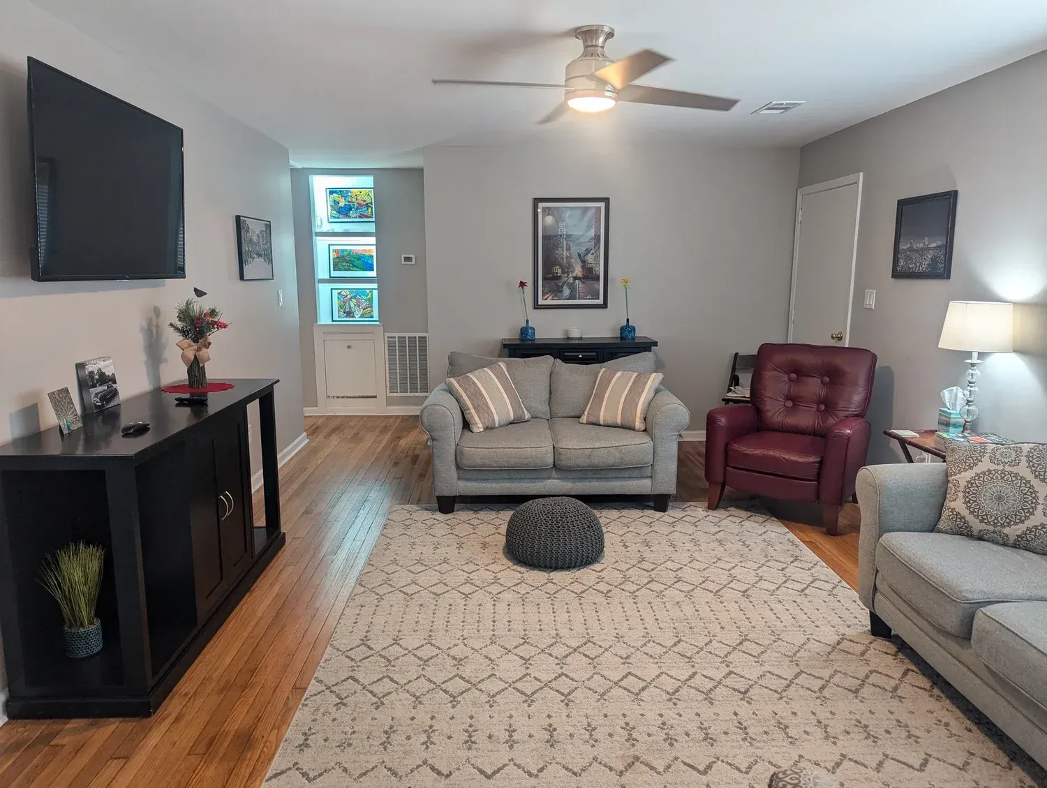 A round table with a floral centerpiece, two stools, two white benches, and a blue armchair under a crystal chandelier.