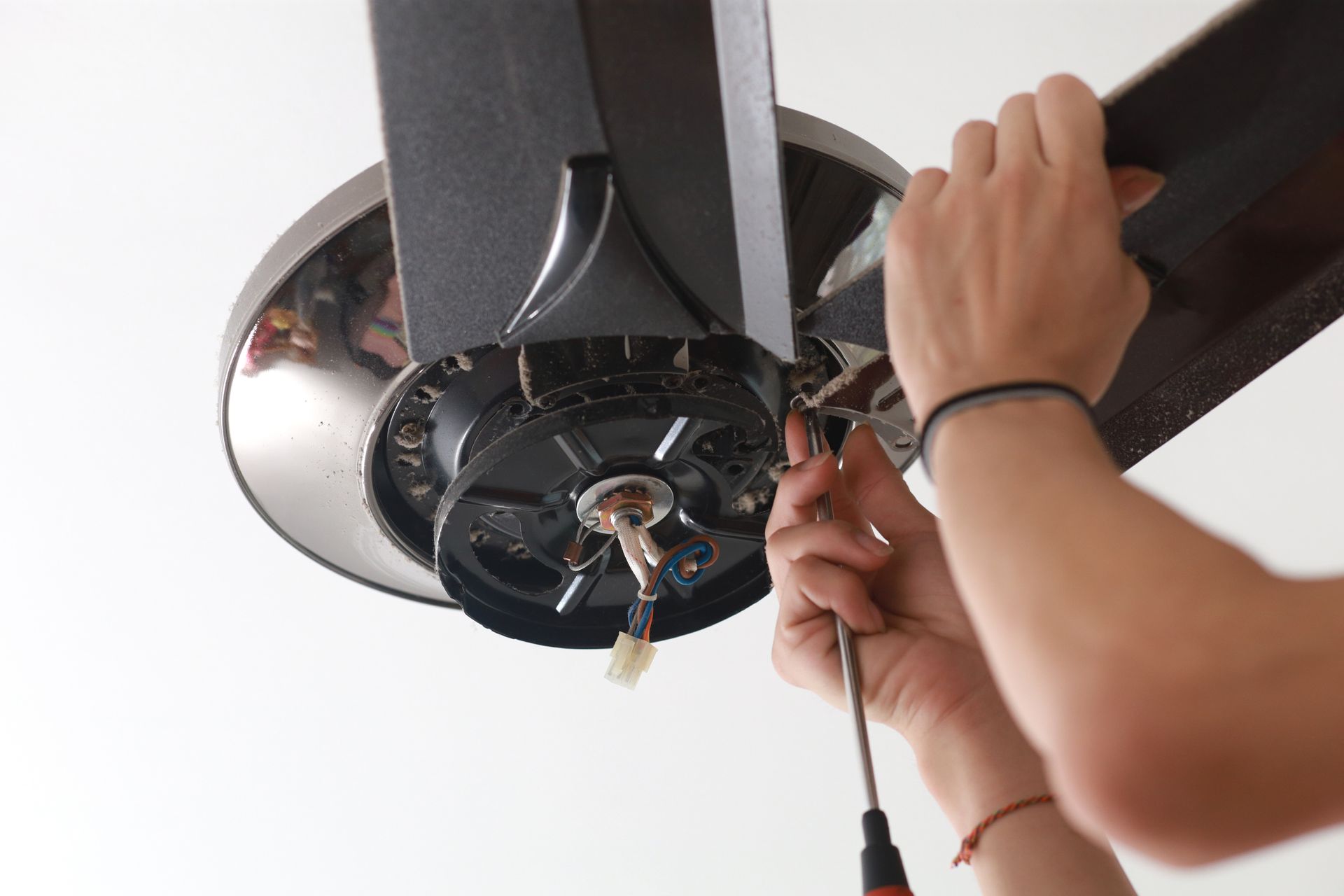 A handyman focused on fixing and installing a ceiling fan in a house.