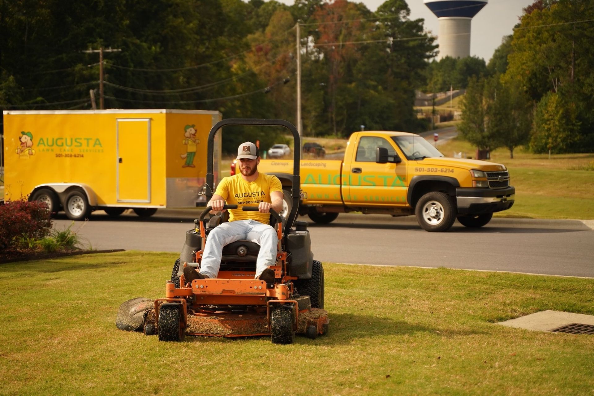 a man is riding a lawn mower in front of a yellow truck .