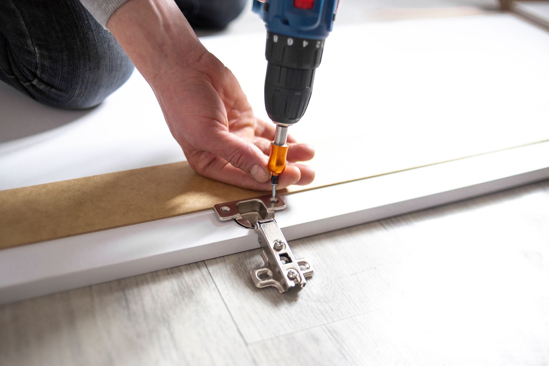 A person is using a drill to install a door hinge on a piece of wood.