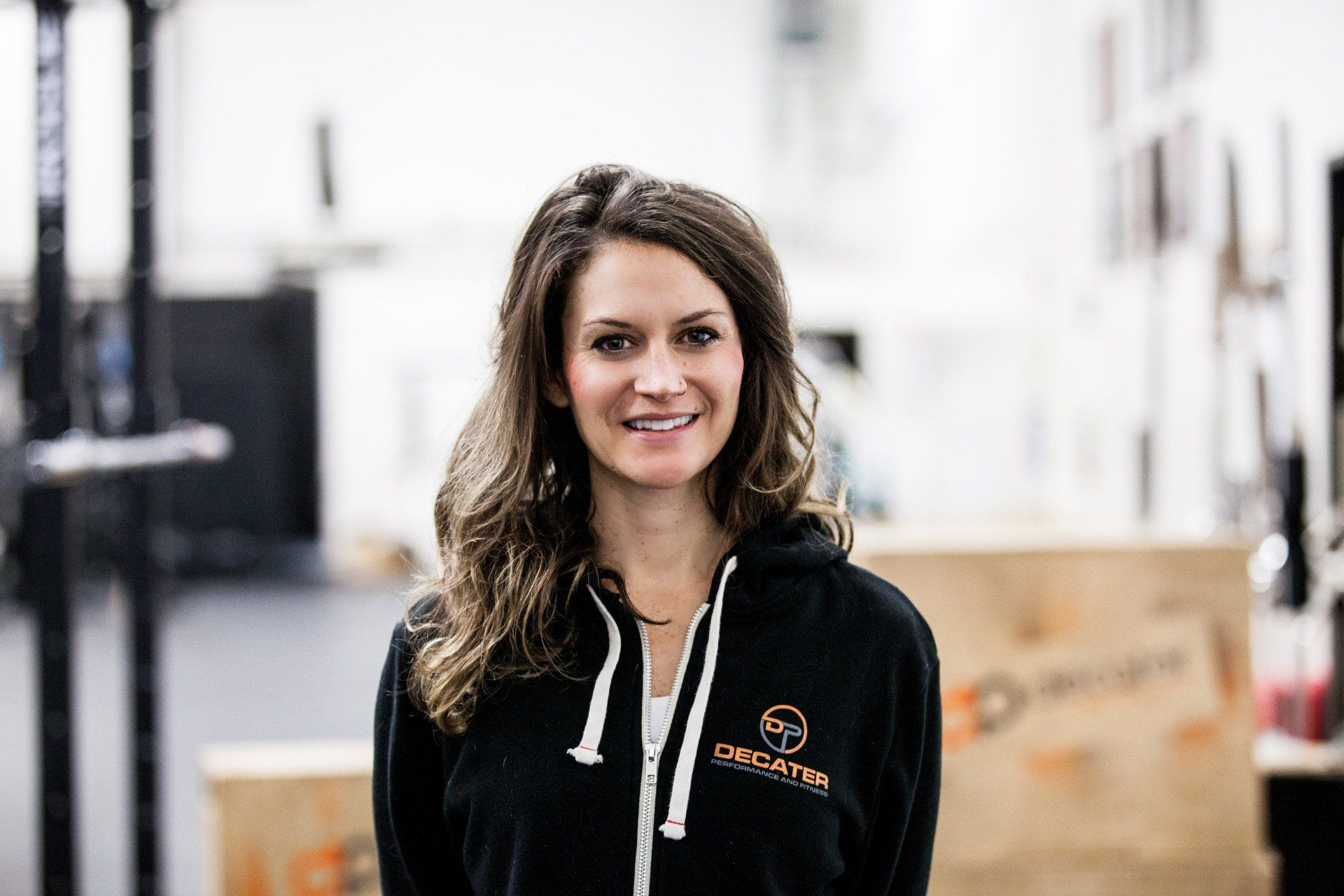 Woman in black hoodie smiling in a gym setting.