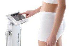 Woman using InBody body composition analyzer, in white shorts and top, touching screen.