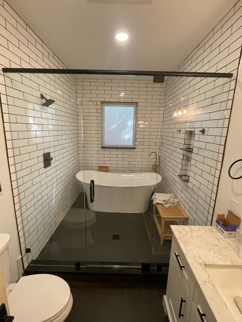 Modern bathroom with white subway tile, black framed glass shower, freestanding tub, and dark gray floor.