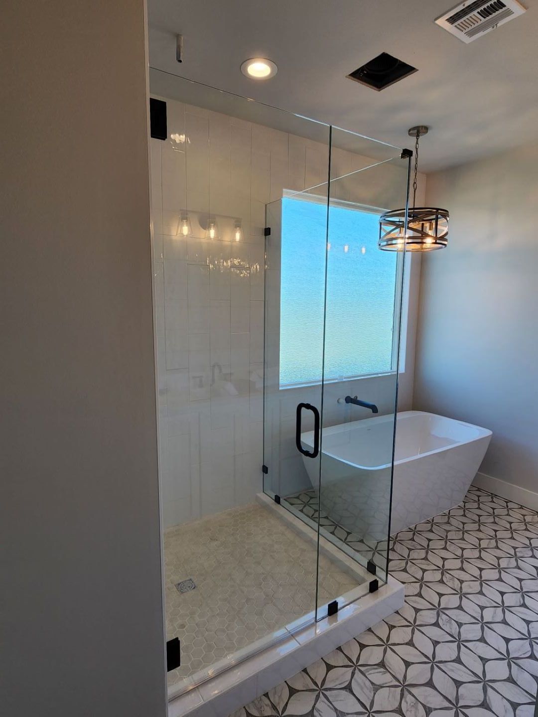Modern bathroom with glass shower, soaking tub, and patterned tile floor.