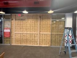 Exterior of a business with boarded-up windows and an exit sign visible. A ladder is in the foreground.