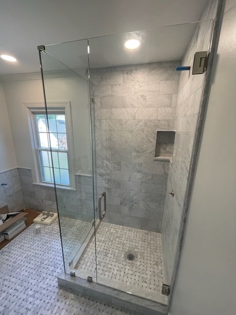 Glass shower enclosure with gray tiled walls and floor, built-in shelf, and small window.