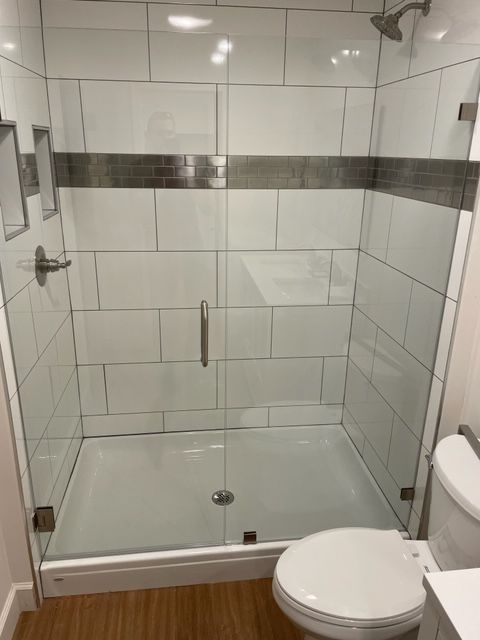 Modern shower stall with white tiles, glass doors, and a decorative gray band.